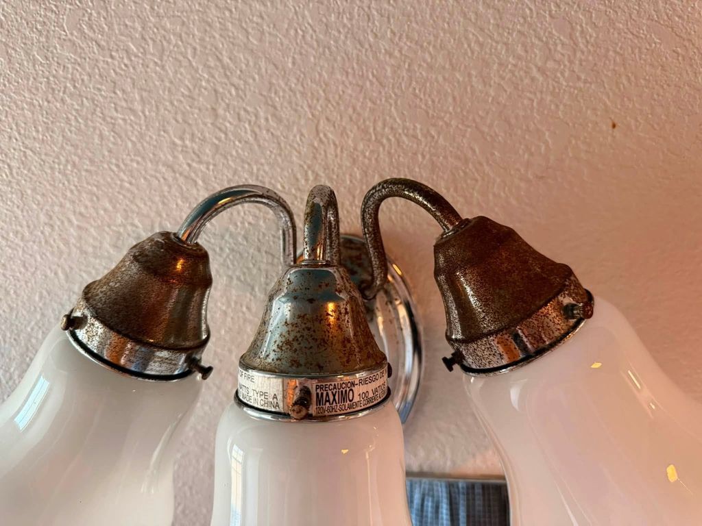 Three-light bathroom fixture before cleaning with residue on the metal shades