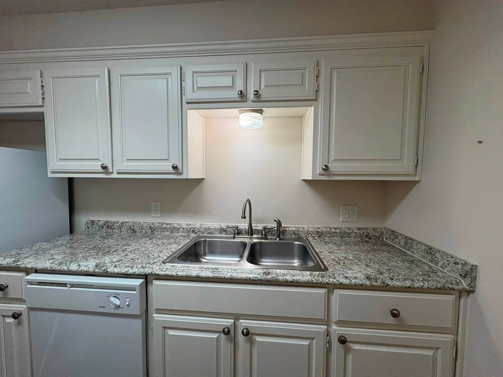 Empty kitchen with white cabinets, granite counter and a stainless steel sink